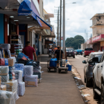 Vista ilustrativa de área comercial de fronteira em Guajará-Mirim, com mercadorias e circulação urbana, sem textos legíveis