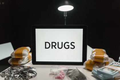 Drogas, dinheiro e algemas dispostos sobre uma mesa sob iluminação intensa.