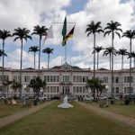 Edifício municipal cercado por palmeiras sob céu nublado.