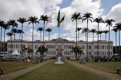 Edifício municipal cercado por palmeiras sob céu nublado.