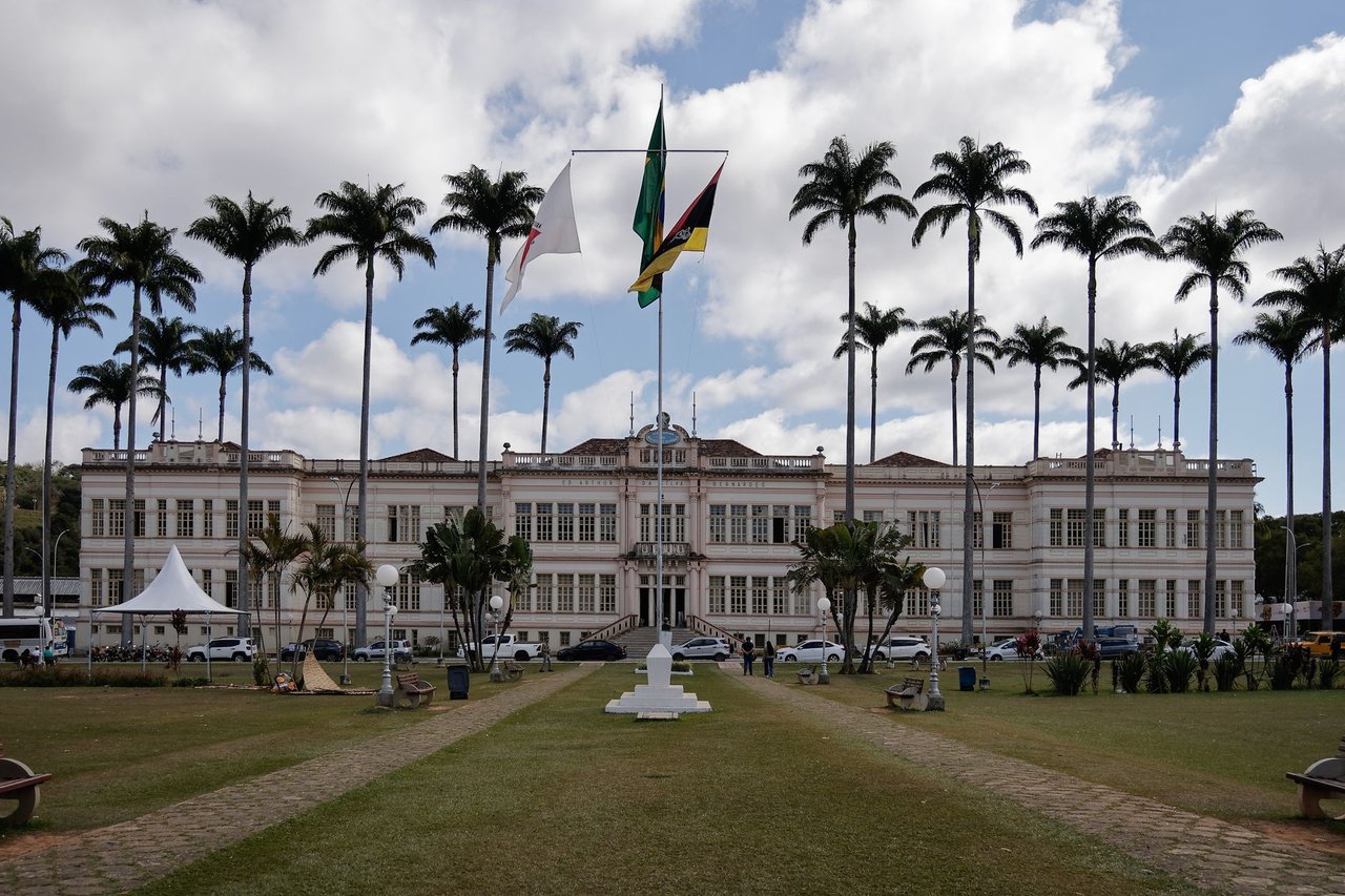 Edifício municipal cercado por palmeiras sob céu nublado.