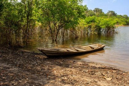 Canoa de madeira junto às margens verdes de um rio na floresta amazônica.