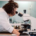 Pesquisadora observa uma amostra ao microscópio em um laboratório.