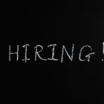 Close-up da palavra “Hiring!” escrita em giz branco sobre um quadro-negro.