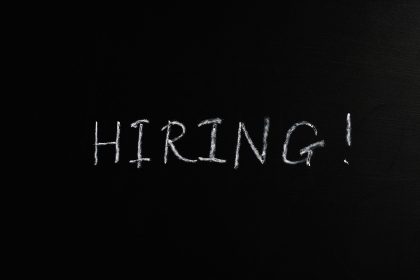 Close-up da palavra “Hiring!” escrita em giz branco sobre um quadro-negro.