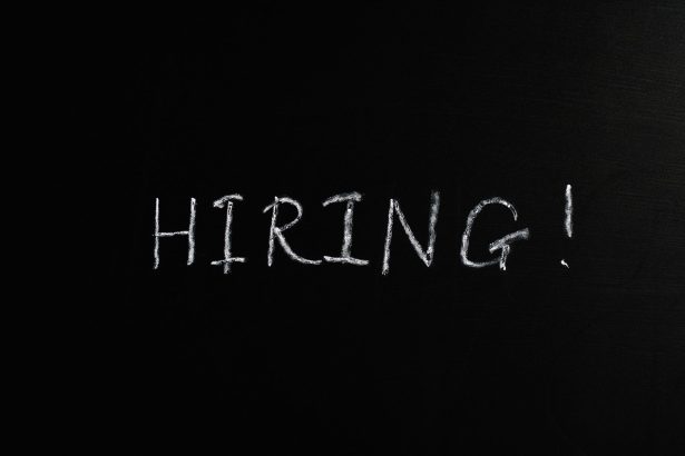 Close-up da palavra “Hiring!” escrita em giz branco sobre um quadro-negro.