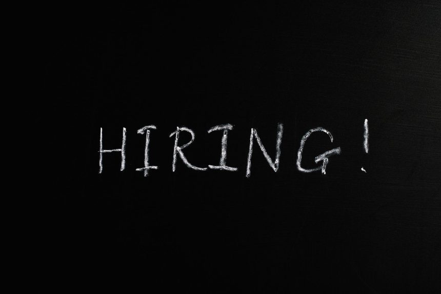 Close-up da palavra “Hiring!” escrita em giz branco sobre um quadro-negro.